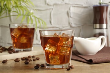 Tasty coffee with ice in glasses and beans on wooden table against light textured background, closeup