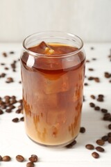 Tasty iced coffee with milk and beans on white wooden table