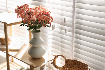 Beautiful pink chrysanthemum flowers in vase on wooden shelf indoors, space for text