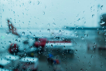 A close up of raindrops on a glass window with a blurred airplane and damp runway in the background