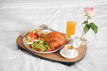 Tray with delicious breakfast and rose on bed in hotel room, closeup