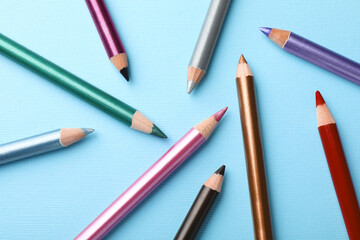 Colorful eye pencils on light blue background, flat lay