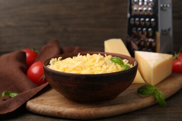Grated and pieces of cheese with basil on wooden table, closeup