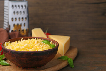 Grated and pieces of cheese with basil on wooden table, closeup. Space for text
