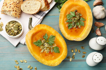 Tasty pumpkin cream soup with seeds, parsley, garlic and bread on light blue wooden table, flat lay