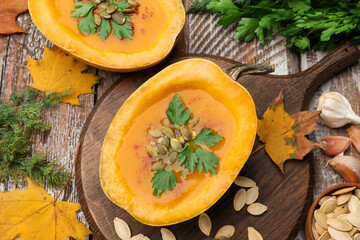 Tasty pumpkin cream soup with seeds, parsley, dill and autumn leaves on color wooden table, flat lay