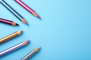 Eye pencils on light blue background, flat lay. Space for text