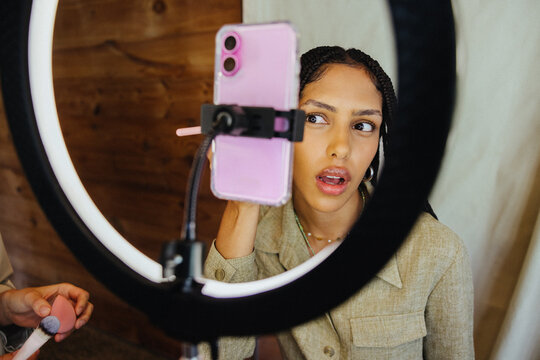 Young woman applies makeup using a ring light and smartphone camera