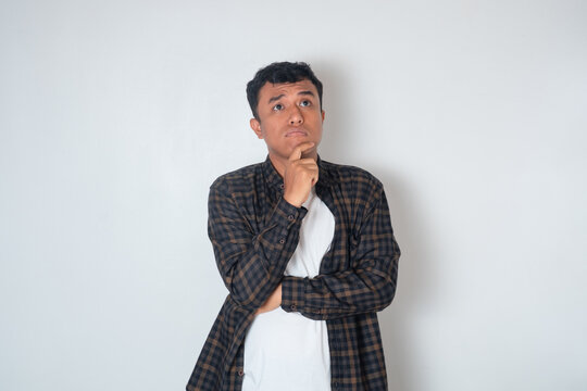 Thoughtful young Asian man in casual shirt touching his chin, looking up, thinking and making decisions isolated on white background - Powered by Adobe