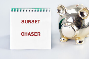 A notebook with the words SUNSET CHASER sits next to a golden piggy bank. Saving up money for trips and adventures, chasing beautiful horizons