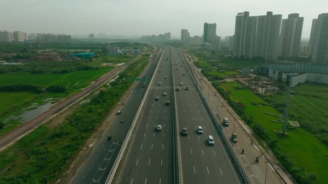 Aerial view of Dwarka Expressway with cars traversing its lanes, framed by the green landscape and buildings, Gurugram, Haryana, India.