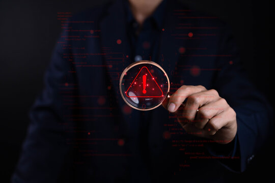 Businessman holding magnifying glass with red warning alert symbol and binary code background, representing cybersecurity risk, data breach detection, and digital system protection concept.