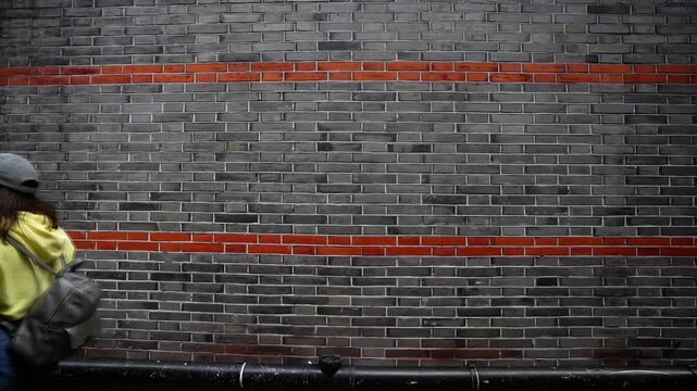 Tourist woman walks past a grey brick wall accented by red trim in the Xintiandi neighborhood. Shanghai, China