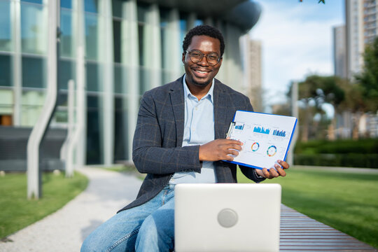 African american businessman presenting data analysis graphs outdoors - Powered by Adobe