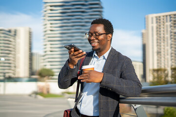 Black businessman using smartphone voice assistant in city