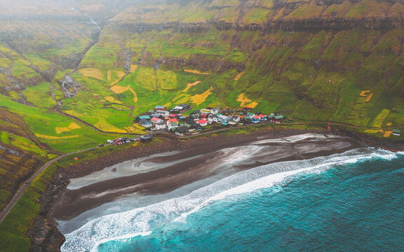 Aerial view of a small village nestled between the stark black sands, emerald slopes, and the turquoise waves of the sea, Tj&Atilde;&cedil;rnuv&Atilde;&shy;k, Streymoy, Faroe Islands.