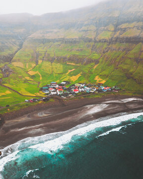 Aerial view of a coastal village nestled between a black sand beach and green cliffs under a misty sky, Tj&Atilde;&cedil;rnuv&Atilde;&shy;k, Streymoy, Faroe Islands.