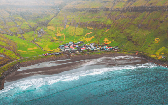 Aerial view of the village nestled between the dark sandy beach and the vibrant green hills, a scene of contrasting beauty, Tj&Atilde;&cedil;rnuv&Atilde;&shy;k, Streymoy, Faroe Islands.