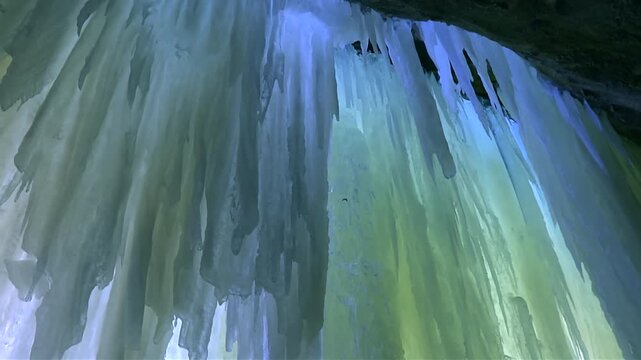 Streaked yellow and blue ice sheets with jagged icicles hang from cave ceiling in close up view, Eben Ice Caves, USA