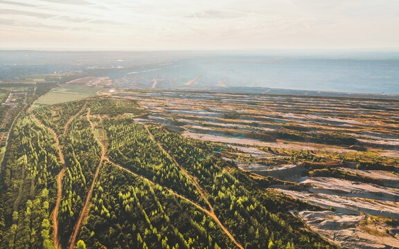 Aerial view of vibrant green forests juxtapose with the stark, textured landscape of the Tagebau Hambach mine under a soft sky., Elsdorf, Nordrhein-Westfalen, Germany.