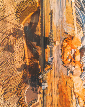 Aerial view of the colossal, earth-moving machinery carving deep furrows into the ochre and umber landscape of Tagebau Hambach, Elsdorf, Nordrhein-Westfalen, Germany.