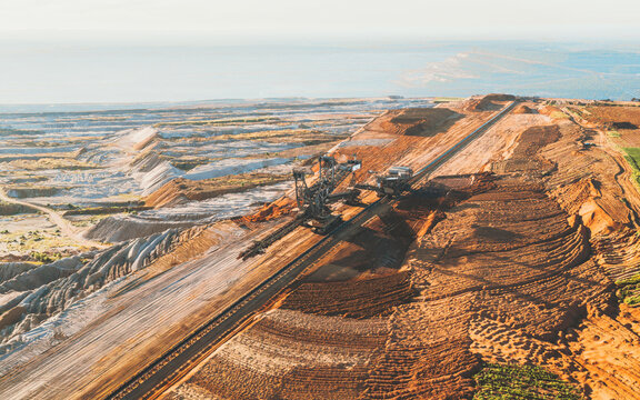 Aerial view of massive excavators carve deep into the layered earth, contrasting sharply with the distant horizon, Tagebau Hambach, Nordrhein-Westfalen, Germany.