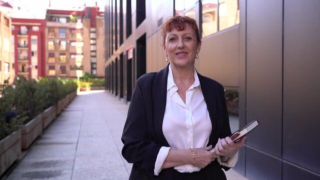 Smiling senior businesswoman standing holding a planner near office building