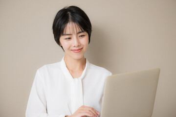 ベージュ背景でパソコンを持つポーズのかわいい黒髪の美人な女性