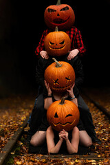 Four friends celebrate Halloween with stacked pumpkins on a railway surrounded by autumn leaves at dusk