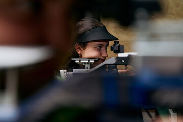 Focused young woman athlete aiming with air rifle, precision shooting sport, concentration and discipline, indoor competition, training for olympic games, competitive spirit, determination. © Minet