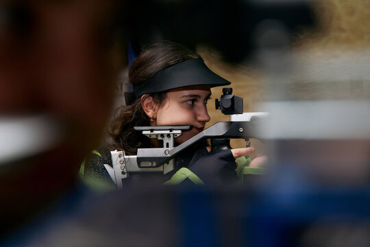 Focused young woman aiming with a rifle, precision sport, competitive shooting, concentration and skill, professional shooter, aiming for success, target practice, determination.