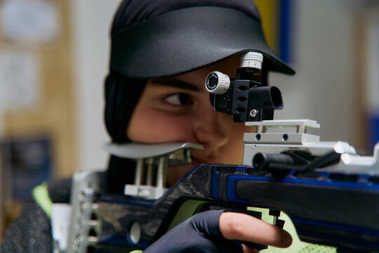 Focused female shooter aiming rifle in target practice, precision sport, competitive shooting, concentration and discipline, indoor shooting range, professional marksman, olympic sport.