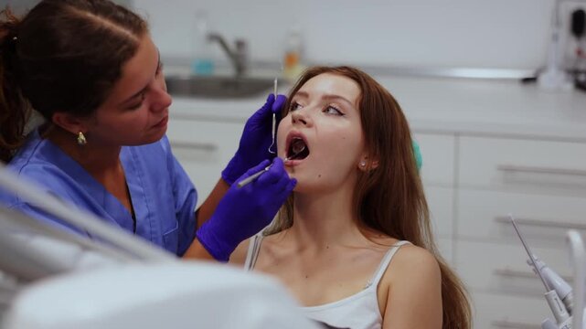 Young woman came for an examination and professional dental hygiene at a dental clinic. Woman dentist carefully examines the teeth of a client. High quality FullHD footage