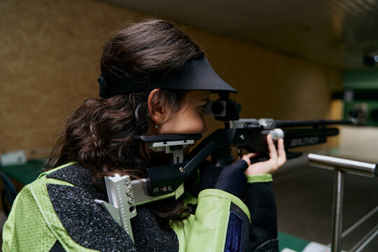 Woman aiming a rifle in shooting sport competition, precision shooting, air rifle shooting, professional shooter, shooting range, focus and concentration, competitive sport, aiming for success.