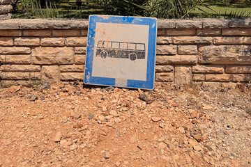 abandoned bus stop sign on the ground leaning against stone brick wall