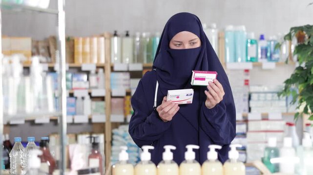 Young woman buyer in hijab chooses box of paracetamol tablets in pharmacy