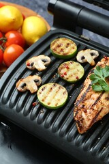 Electric grill with tasty chicken fillet, mushrooms and products on table against grey background, closeup