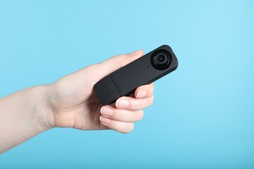 Woman with hidden spy camera on light blue background, closeup