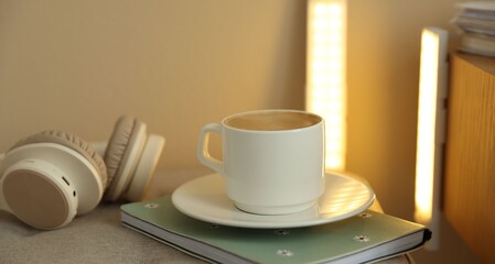 Coffee, notebook, headphones on pouf and portable LED lamps at home, closeup