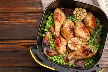 Air fryer basket with grilled chicken drumsticks, spices and green peas on wooden table, top view. Space for text