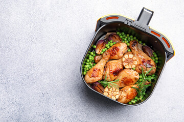 Air fryer basket with grilled chicken drumsticks, spices and green peas on grey table, top view. Space for text