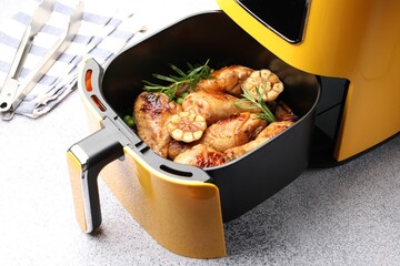 Air fryer with grilled chicken drumsticks, spices and green peas on grey table, closeup