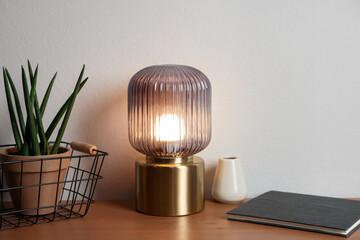 Stylish lamp, vase, houseplant and book on wooden table near white wall indoors