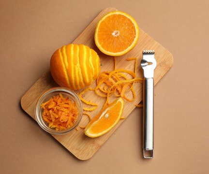 Orange zest, fresh fruits and zester tool on beige background, top view