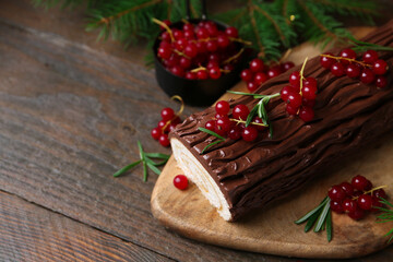 Delicious Yule log (traditional Christmas cake) with redcurrant and fir tree branches on wooden table, closeup. Space for text