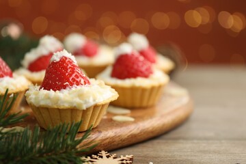 Christmas food. Tasty tartlets with strawberries, whipped cream, coconut flakes and decor on wooden table against background with blurred lights, space for text. Bokeh effect
