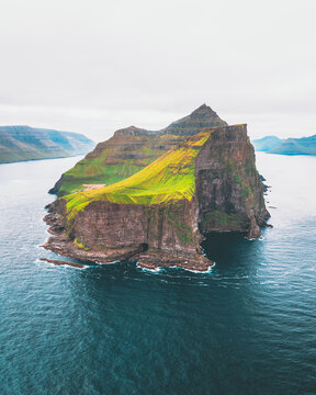 Aerial view of emerald green grass contrasting with the dark, rugged cliffs of Kallur Lighthouse, surrounded by the deep blue sea, Kallur Lighthouse, Nor&Atilde;&deg;oya, Faroe Islands.