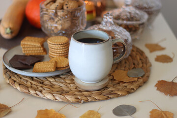 Lit candles, cookies, chocolate, nuts, tea, wine, pumpkins, books, reading glasses and autumn leaves on the table. Autumnal hygge at home. Selective focus.
