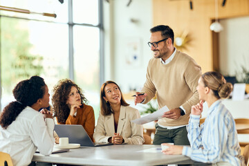 Collaborative Business Meeting With Presenter Standing, Diverse Team Of Professionals At Modern Bright Office Today