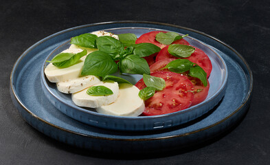 Classic Caprese salad with sliced ​​fresh tomatoes, mozzarella and basil leaves on a blue...